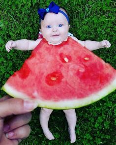 a baby in a watermelon dress holding up a piece of watermelon