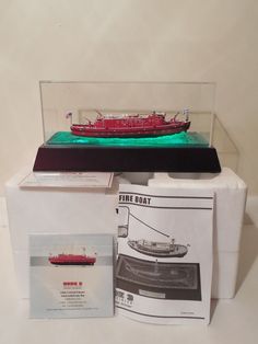 a red boat in a glass case on top of a white box with information about it