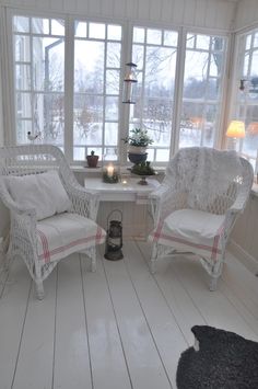 two white wicker chairs sitting in front of a window next to a table with candles on it