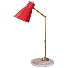 a red lamp on a white background with a gold base and a light bulb that is turned on