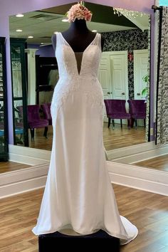 a white wedding dress on display in front of a mirror with purple chairs behind it