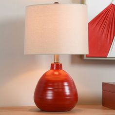 a red lamp sitting on top of a wooden table next to a framed art piece