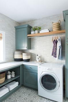 a washer and dryer in a small room with green cabinets, white tile flooring and open shelving