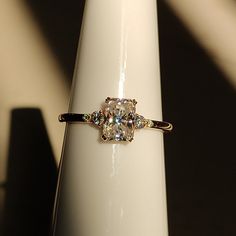 an engagement ring with three stones on it sitting on top of a white pedestal in the sunlight