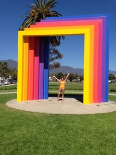 a woman standing in front of a giant rainbow colored structure with her arms raised up