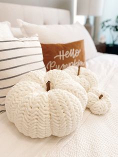 two knitted pumpkins sitting on top of a bed next to a throw pillow