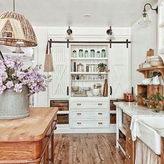 an old fashioned kitchen with white cabinets and wood floors, flowers in a bucket on the counter