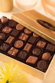 a box of assorted chocolates sitting on a table next to a yellow flower