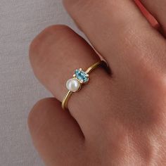 a woman's hand with a ring on it that has an aqua and white pearl