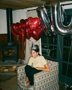 a woman sitting in a chair with balloons and a birthday hat on her head