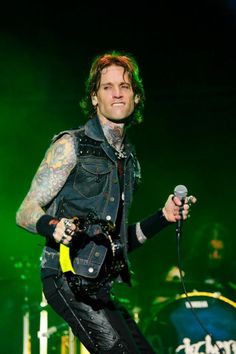 a man with tattoos on his arm holding a microphone and standing in front of a green light