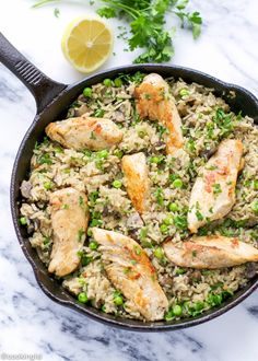 chicken and rice with peas in a skillet on a marble countertop next to lemon wedges