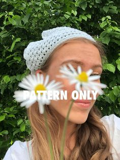 a woman wearing a crochet hat with daisies in front of her face