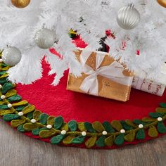 a christmas tree skirt with presents on it and ornaments around the tree in gold, white and green