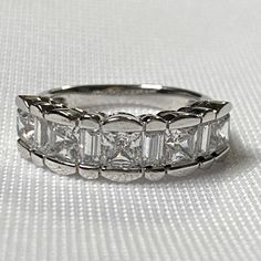 a wedding ring with five princess cut diamonds on the sides and four baguetts in the middle