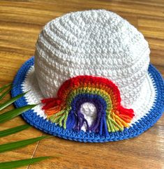 a white crocheted hat with a rainbow decoration on the brim, sitting on a wooden surface