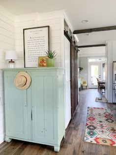 a blue cabinet with a hat on top of it in a room that has wood floors and white walls