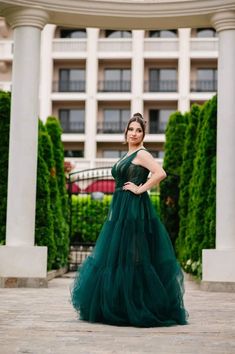 a woman standing in front of a building wearing a dark green gown and posing for the camera