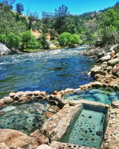 there is a hot tub in the middle of some rocks and water with trees around it