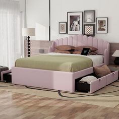 a pink bed with two drawers underneath it in a room next to pictures on the wall