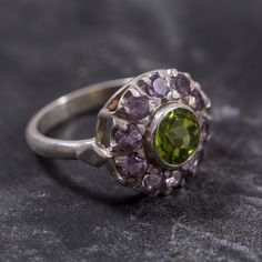 Peridot Ring set with Natural Peridot in a diamond cut & natural green color, at size 7mm together with Natural Amethyst at size 3mm each (2.3 Cts combined) from Brazil.Solid 925 Sterling Silver ☞ made to last.Click here for ☞ Matching PendantClick here for ☞ Matching EarringsClick here for ☞ Flower Collection Details:• Natural Peridot & Amethyst sourced from Brazil• Peridot: 7mm, 1.3 Cts, diamond cut• Amethyst: 3mm each, 1 Ct total, diamond cut• Dimensions: Band width ≈ 2.3mm, thickness ≈ 1.3mm Green Sterling Silver Amethyst Ring For Wedding, Green Amethyst Rings In Fine Jewelry Style, Green Amethyst Birthstone Ring In Fine Jewelry Style, Green Amethyst Ring With Center Stone For Wedding, Green Amethyst Birthstone Ring, Wedding Amethyst Ring With Green Center Stone, Fine Jewelry Green Amethyst, Green Amethyst Fine Jewelry, Green Peridot Ring With Center Stone