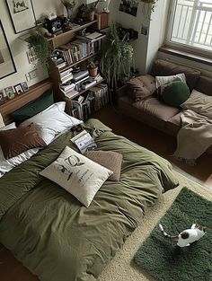 a bed with green sheets and pillows in a room filled with bookshelves, couches, and pictures on the wall