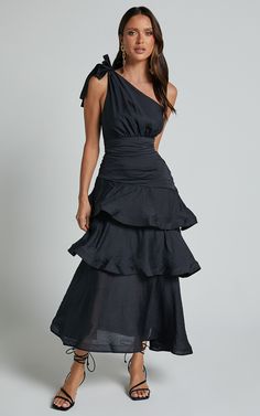 a woman wearing a black dress with one shoulder and tiered ruffles on the bottom