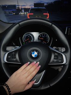 a woman's hand is on the steering wheel of a bmw car at night