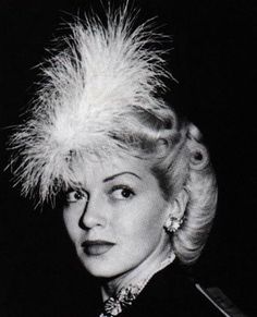 a black and white photo of a woman wearing a feathered hat