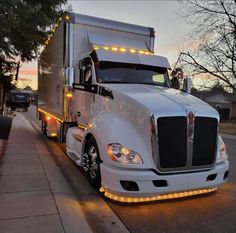 a white semi truck is parked on the side of the road with its lights on