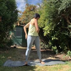 a woman standing on top of a yoga mat in the middle of a park area