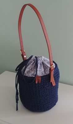 Navy Bucket Bag. Crocheted navy blue bucket bag, cotton blue and white fabric lining, inside pockets, drawstring closure, and brown leather buckle strap.  Dimensions: 23 inches round, 7.25 inches deep, 12 inch strap drop.  Surface washable.  Thank you for visiting YellowRoseRetail.com! Casual Bucket Bag With Leather Trim, Blue Bags With Leather Trim For Shopping, Blue Leather Trim Shopping Bag, Blue Shoulder Bag With Leather Trim For Everyday, Blue Shoulder Bag With Leather Trim For Daily Use, Blue Leather Trim Bags For Shopping, Everyday Blue Shoulder Bag With Leather Trim, Daily Use Bucket Hobo Bag With Leather Trim, Blue Leather Handle Bucket Bag