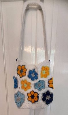 a crocheted purse hanging from a hook on a white door handle with blue, yellow and orange flowers