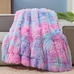 a pink and blue blanket sitting on top of a couch next to a white chair