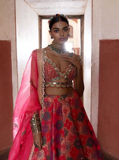 This exquisite banarasi lehenga, inspired by the elegance of jharokhas, is beautifully paired with a coral plunging V-neck sheeted blouse and a flowing organza dupatta. Delicately highlighted with cut mirrors and pearls, the ensemble radiates sophistication and charm. A stylish belt cinches the waist, enhancing the silhouette and completing this stunning look with a perfect blend of tradition and contemporary flair. Chanderi Lehenga, Silk Lehenga, Organza Dupatta, Silk Blouse, Lehenga, Coral, Cute Outfits, V Neck, Couture