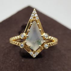 a gold ring with a pear shaped white stone surrounded by small round brilliant cut diamonds