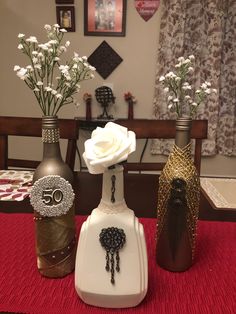 three vases with flowers in them sitting on a red tablecloth covered dining room