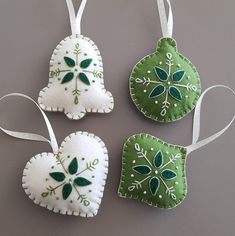 three ornaments are hanging on a gray wall and one is decorated with green leaves, the other has white trim