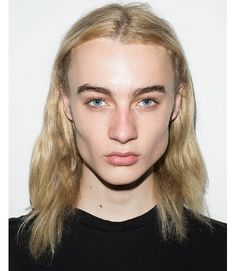 a woman with long blonde hair and blue eyes looks at the camera while wearing a black t - shirt