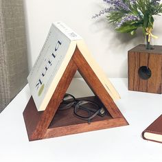 a wooden triangle with a book and glasses on it next to a flower pot in the corner