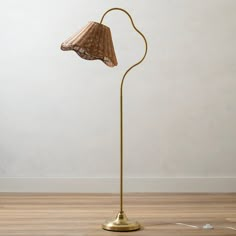 a gold floor lamp with a brown shade on it's head and a white wall in the background