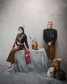 two people standing next to each other in front of a table with vases on it