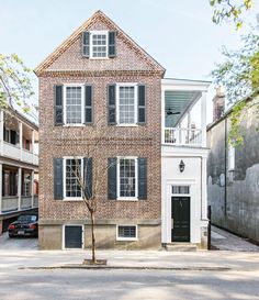 an old brick house with black shutters on the front and second story, along side a street