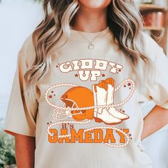 Gear up for game day with our Women's Giddy Up Gameday apparel, specially designed for fans of your favorite big orange football team! Perfect for the football season frenzy, this versatile design is available for toddlers, youth, and adults of all sizes. Show your team spirit in style and make every game day a memorable one with our exclusive collection. Comfort Colors introduces the "Comfort Colors 1717" garment-dyed t-shirt; a fully customizable tee made 100% with ring-spun cotton. The soft-washed, garment-dyed fabric brings extra coziness to your wardrobe while the relaxed fit makes it an excellent daily choice. The double-needle stitching throughout the tee makes it highly durable while the lack of side-seams helps the shirt retain its tubular shape. Discover all 58 colors in our Comf Orange Short Sleeve T-shirt For Game Day, Orange Cotton T-shirt For Game Day, Orange Team Spirit Tops For Sports Events, Orange Tops For Sports Events With Team Spirit, Orange Crew Neck T-shirt For Game Day, Orange Tops For Game Day With School Spirit, Collegiate Orange Tops For Game Day, Orange Tops For Fan Gear With Team Spirit, Orange Team Spirit T-shirt With Letter Print