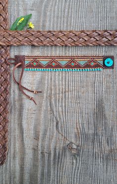 a brown belt with blue beads and a green flower on the end is sitting on a wooden surface