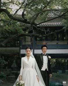 a man and woman dressed in formal wear standing next to each other under a tree