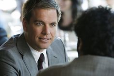 a man in a suit and tie talking to another man at a table with other people