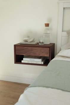 a nightstand with two books on it next to a bed