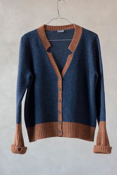 a blue and brown cardigan sweater hanging on a hanger with a white wall in the background