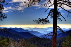 a view of the mountains and trees from a high point on a sunny day with clouds in the sky